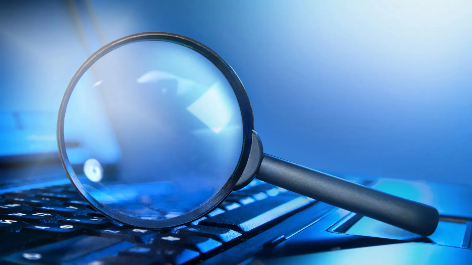 Lupe auf einer blau beleuchteten Laptop-Tastatur