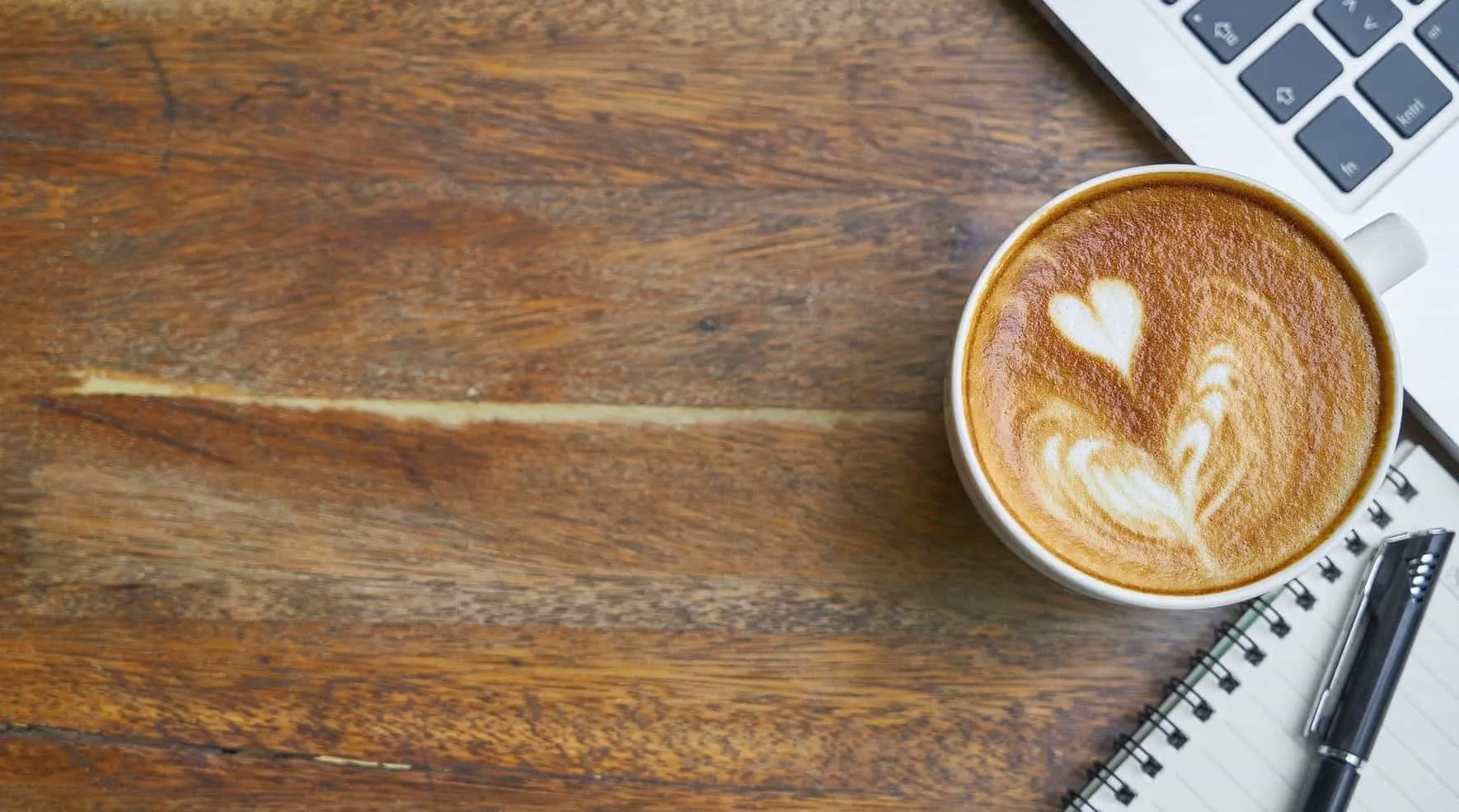 Cup of cappuccino with a heart in the milk foam next to a notepad and laptop – Java 11 Features
