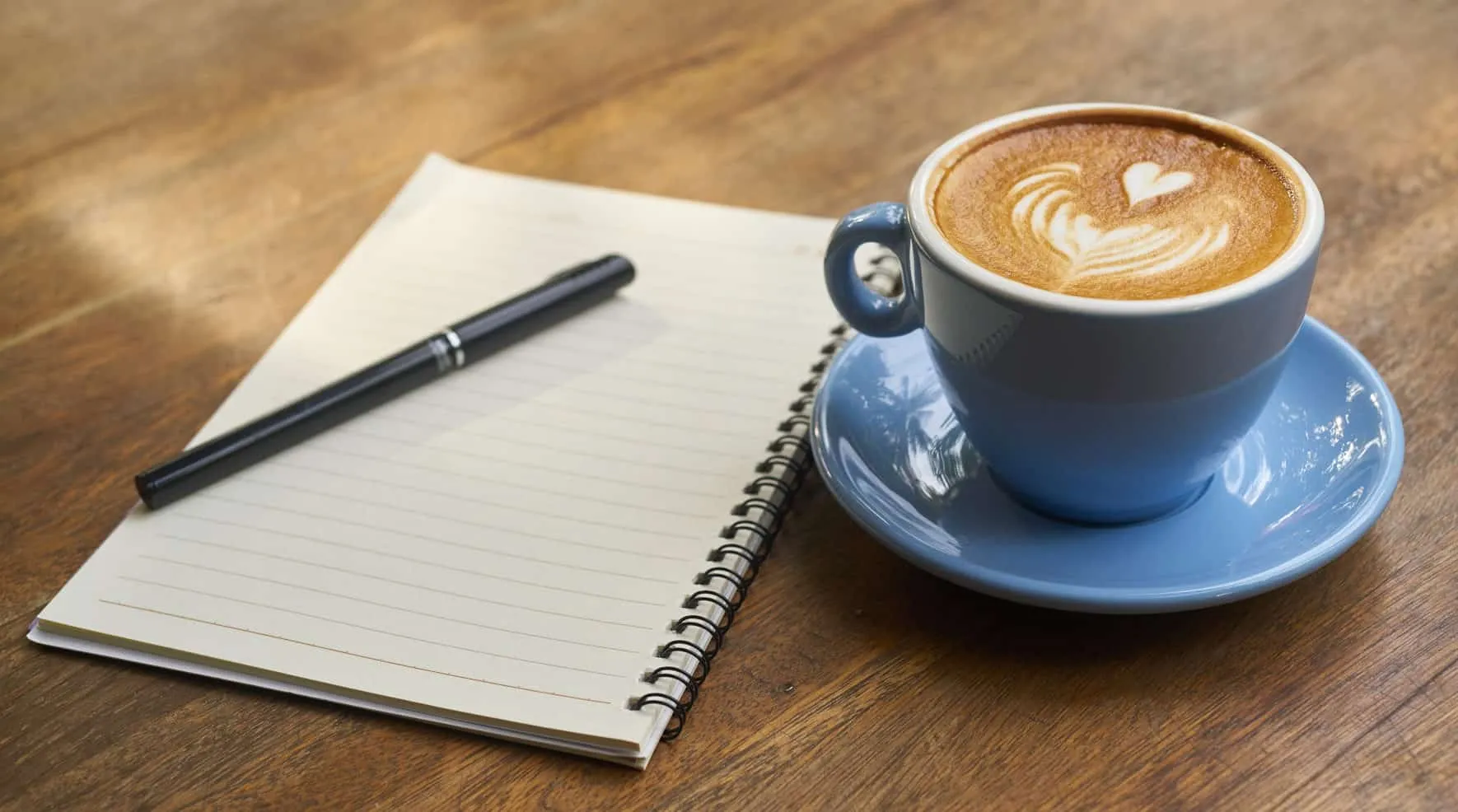 Blue cup of cappuccino next to an open notebook and a fountain pen – Java 14 Features