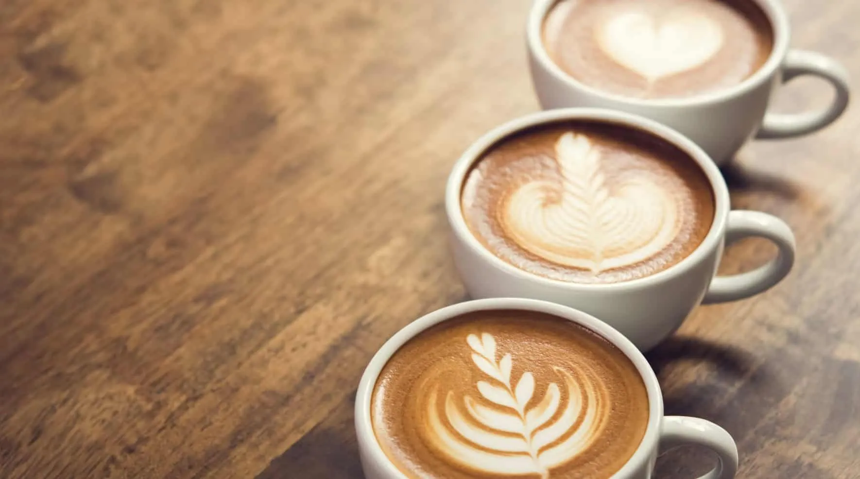 Three cups of cappuccino with latte art on a wooden table – Java 23 Features