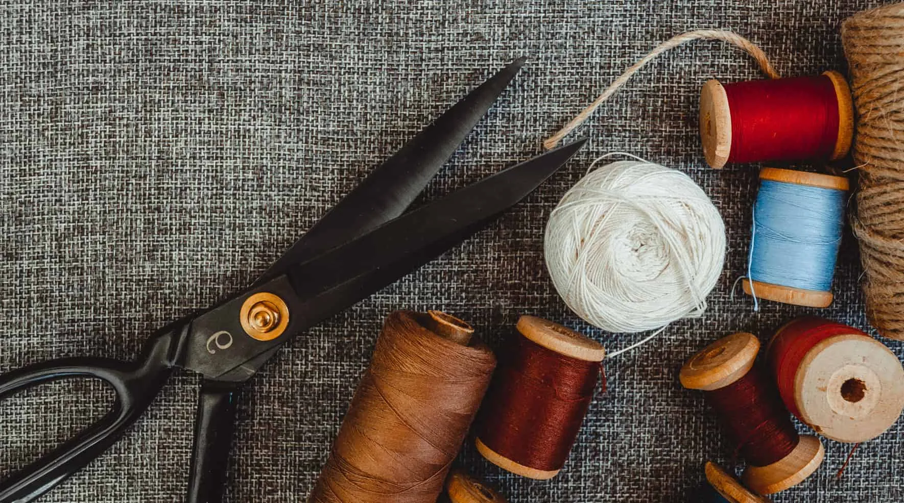 Scissors, spools of thread and yarn on coarse fabric