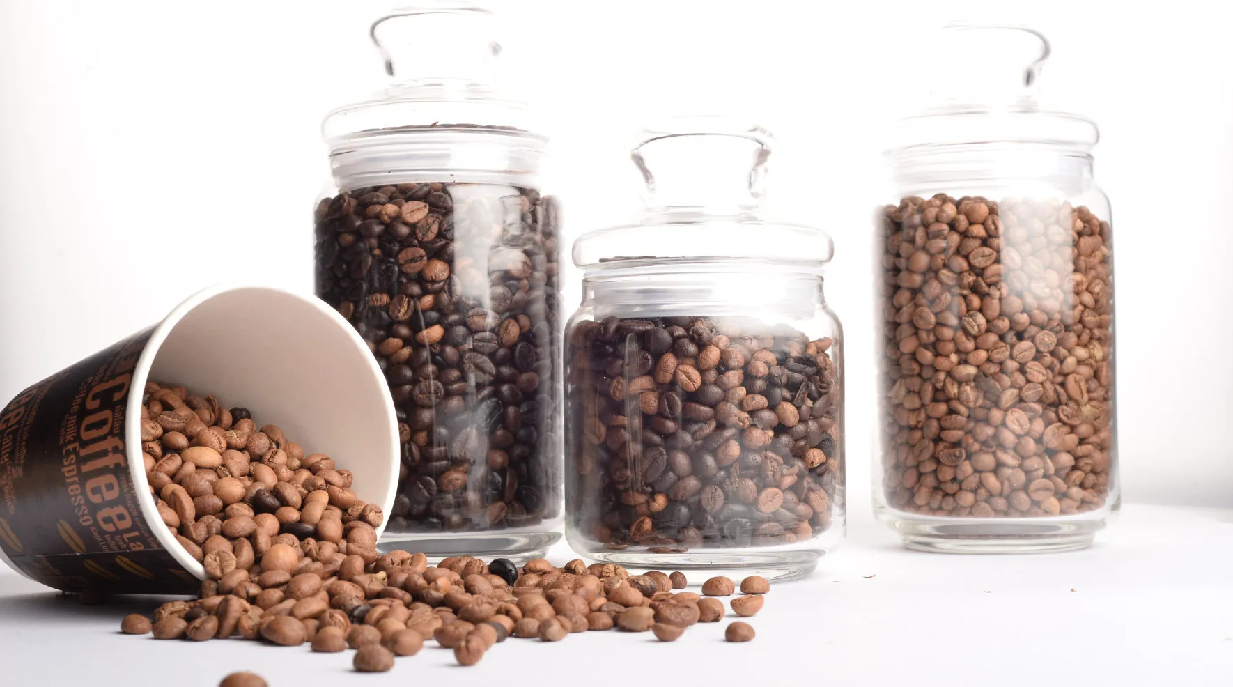Storage jars of coffee beans next to a tipped-over cup